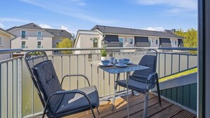 Un balcon avec deux chaises et une table, un pot de fleurs et une vue sur les maisons voisines.