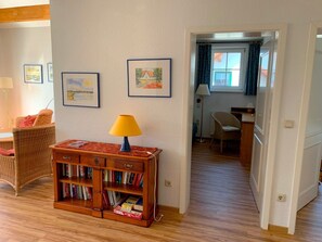 Una habitación con una estantería de madera, una lámpara, cuadros en la pared y un umbral que da a otra habitación.