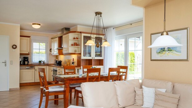 Eine moderne Küche mit Holzschränken, ein Essbereich mit Tisch und Stühlen sowie ein Wohnzimmer mit Sofa und einem Bild an der Wand.