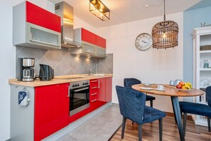 A modern kitchen with red and grey cabinetry, a built-in oven, and a dining area with a round table and blue chairs.