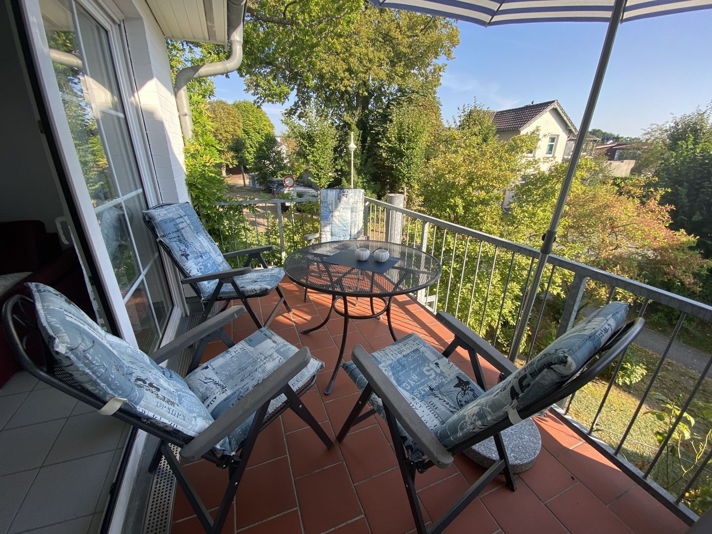 Un balcon avec une table ronde et quatre chaises, chacune agrémentée d’un coussin à motifs de journal.