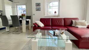 Un salon moderne avec un canapé en cuir rouge, une table basse en verre et un coin repas comprenant des chaises et une table.