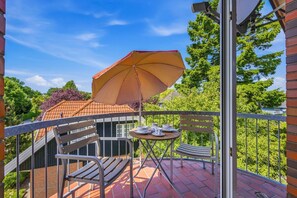 A balcony with a table and chairs, a table set with cups and saucers, and a large umbrella.