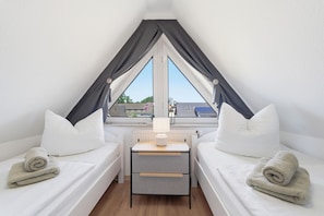 A small, triangular room with two beds, a nightstand, and a window.