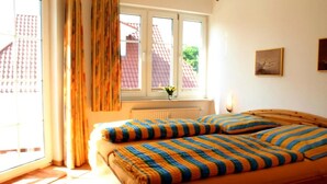 Une chambre à coucher avec un lit en bois, une literie à rayures, une fenêtre avec des rideaux, un radiateur et une lampe fixée au mur.