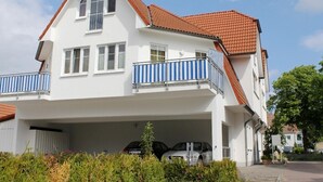 Une maison à deux étages, avec un toit recouvert de tuiles rouges, des murs extérieurs blancs et un garage fermé.