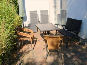 Eine Terrasse im Freien mit Tisch, Stühlen und einer Bank, sowie eine Wand mit Fenstern.