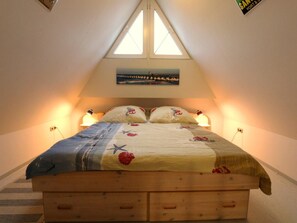 Ein Schlafzimmer mit schrägem Dach, einem Bett mit blumigem Überwurf, zwei Nachttischlampen und einem Gemälde über dem Bett.