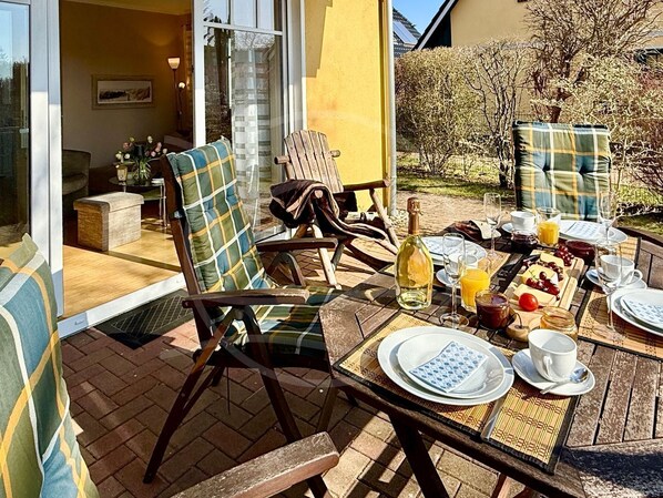 Un espace extérieur aménagé pour prendre les repas, avec des chaises en osier et une table dressée pour le petit-déjeuner.