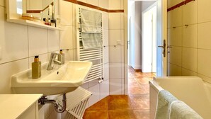 Une salle de bain équipée d’un lavabo, d’un miroir, d’un porte-serviettes et d’une porte donnant sur une autre pièce.