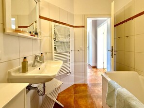 Une salle de bain équipée d’un lavabo, d’un miroir, d’un porte-serviettes et d’une porte donnant sur une autre pièce.