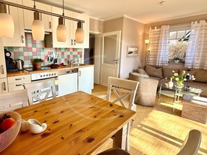 Une cuisine moderne avec des meubles blancs, une table à manger en bois et un coin salon comprenant un canapé et une table basse.