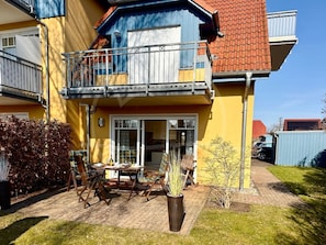 Una casa de dos pisos con un balcón, un patio con muebles de exterior y un pequeño jardín.