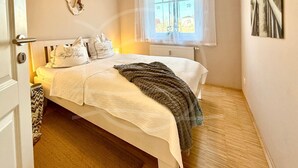 Une chambre à coucher comprenant un lit, des oreillers, une couverture, un radiateur, une fenêtre avec des rideaux et un élément de décoration fixé au mur.