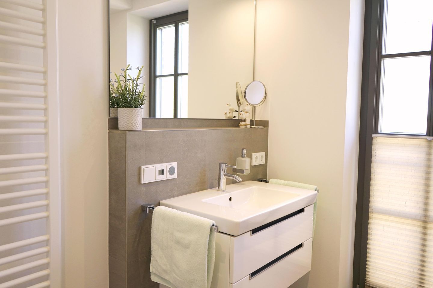 Un baño con un lavamanos blanco, un espejo, una toalla y una planta en maceta.