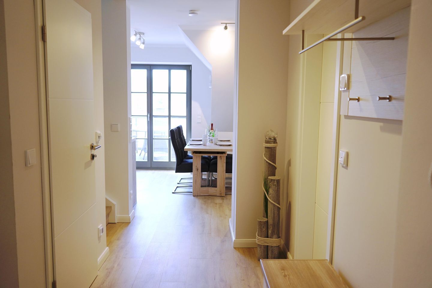 Un couloir mène à une salle à manger équipée d’une table et de chaises, dotée d’un plancher en bois et offrant une vue à travers une porte vitrée.
