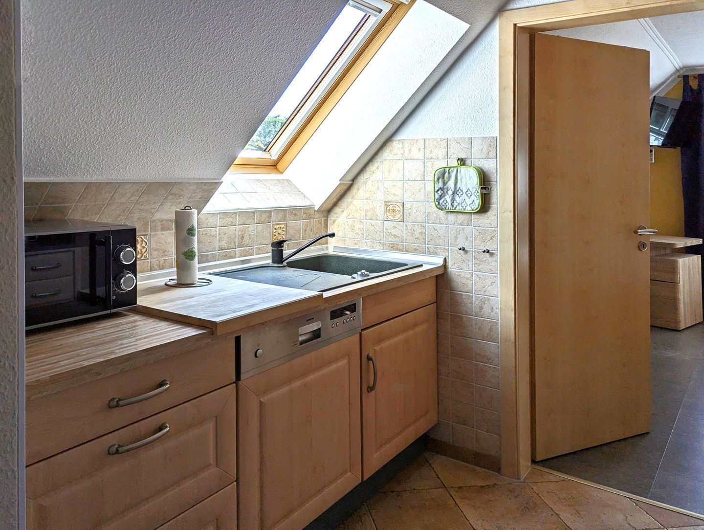 A kitchen with a skylight, a microwave, a sink, and wooden cabinets.