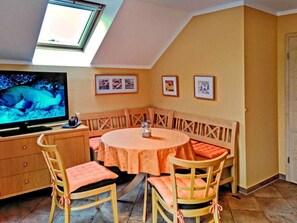 Un comedor con una mesa redonda, sillas de madera, un televisor y cuadros en la pared.