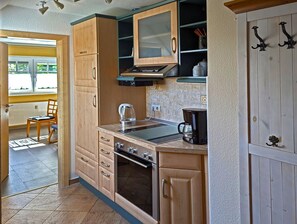 Una cocina con armarios de madera, estufa, cafetera y ventana con vistas.