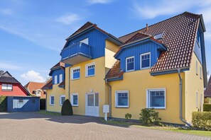 Ein mehrstöckiges Wohngebäude mit gelber Fassade, blauen Akzenten und einem roten Ziegeldach.