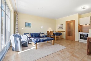 A cozy living room with a sofa, chairs, a dining table, and a kitchen area with a stove.