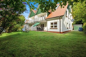 Ein zweigeschossiges Haus mit Balkon, Rasen und Gartenhaus.