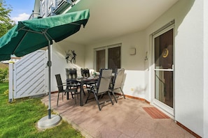 An outdoor patio with a table and chairs, a green umbrella, and a sliding glass door. - Sobek Vacation Apartment - Bright first-floor apartment with a furnished, covered terrace (Zingst)