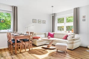 Ein modernes Wohnzimmer mit Essbereich, großen Fenstern und Blick auf Grünflächen.