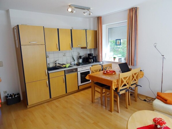 A compact kitchen with wooden cabinets, a dining table, and a laptop on the table.