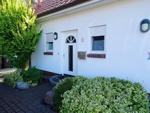 Uma casa branca com porta preta, duas janelas e uma caixa de correio.