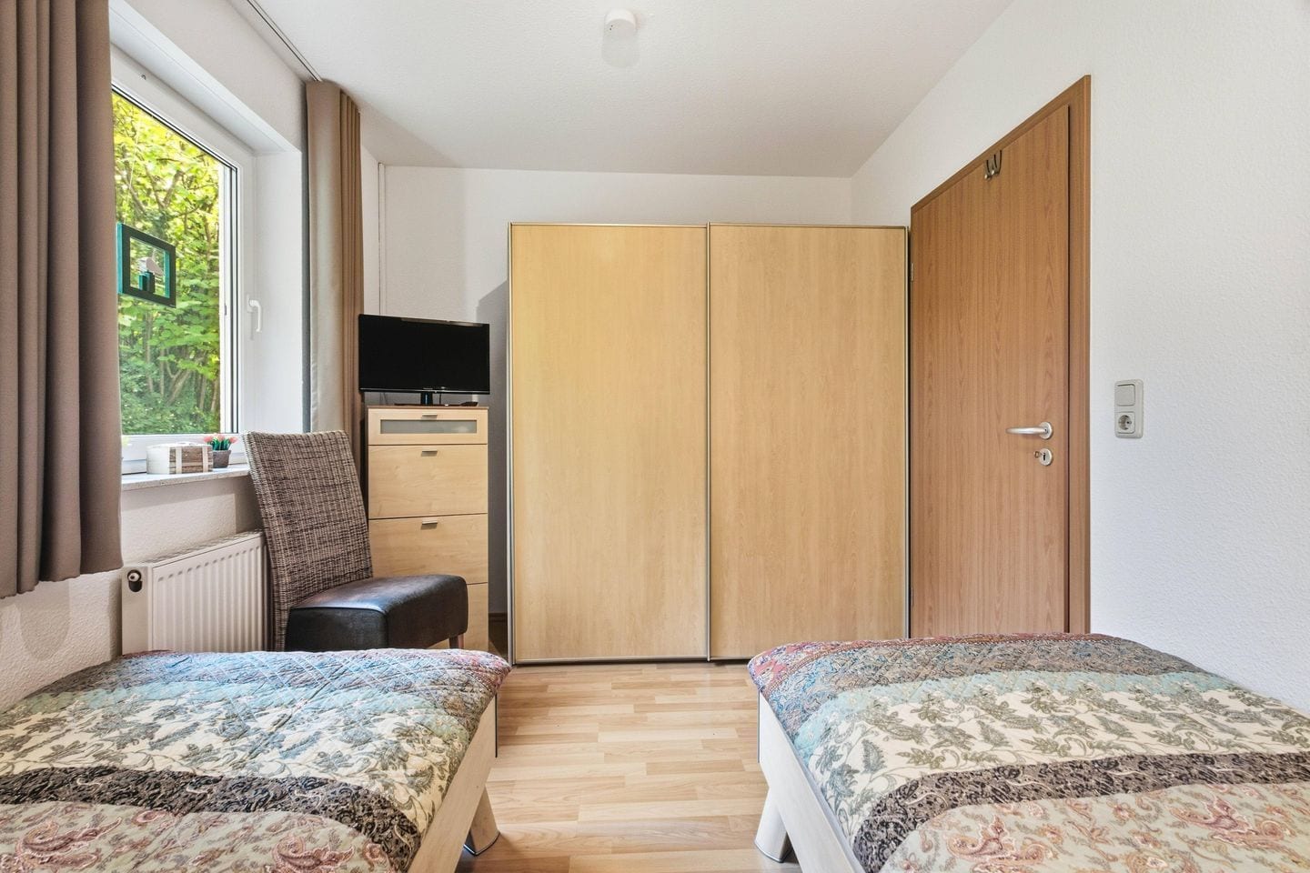 A bedroom with two beds, a dresser, a television, and a wardrobe.