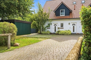 A house with a paved driveway, a green fence, and a well-maintained garden. - Sobek Vacation Apartment - Bright first-floor apartment with a furnished, covered terrace (Zingst)