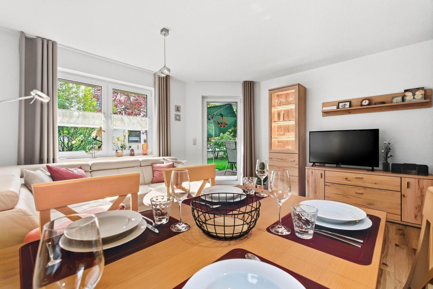 A modern living room with a dining area, a television, and a view of a garden.