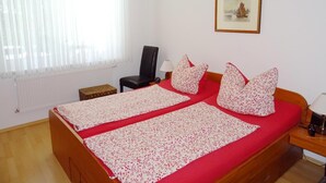 Cama doble con ropa de cama floral, una silla, una mesita, una lámpara y un cuadro en la pared.