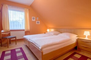Une chambre à coucher comprenant un lit, deux tables de chevet, une chaise, une fenêtre avec des rideaux et un radiateur.