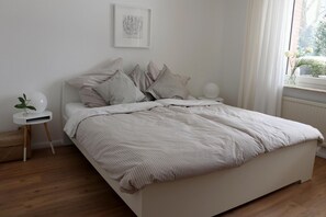 Et minimalistisk soveværelse med seng, sengebord og et vindue med gardiner.