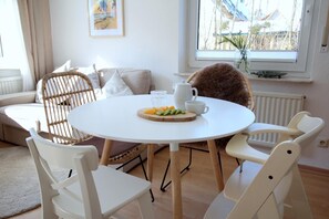 Et rundt spisebord med hvide stole, en hvid kande, et glas og en tallerken med frugt.