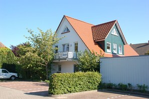 A two-story building with a red-tiled roof, a balcony with a railing, and a white fence in the foreground. - Comfortable vacation apartment with terrace and garden in a central location in Zingst - (Zingst)