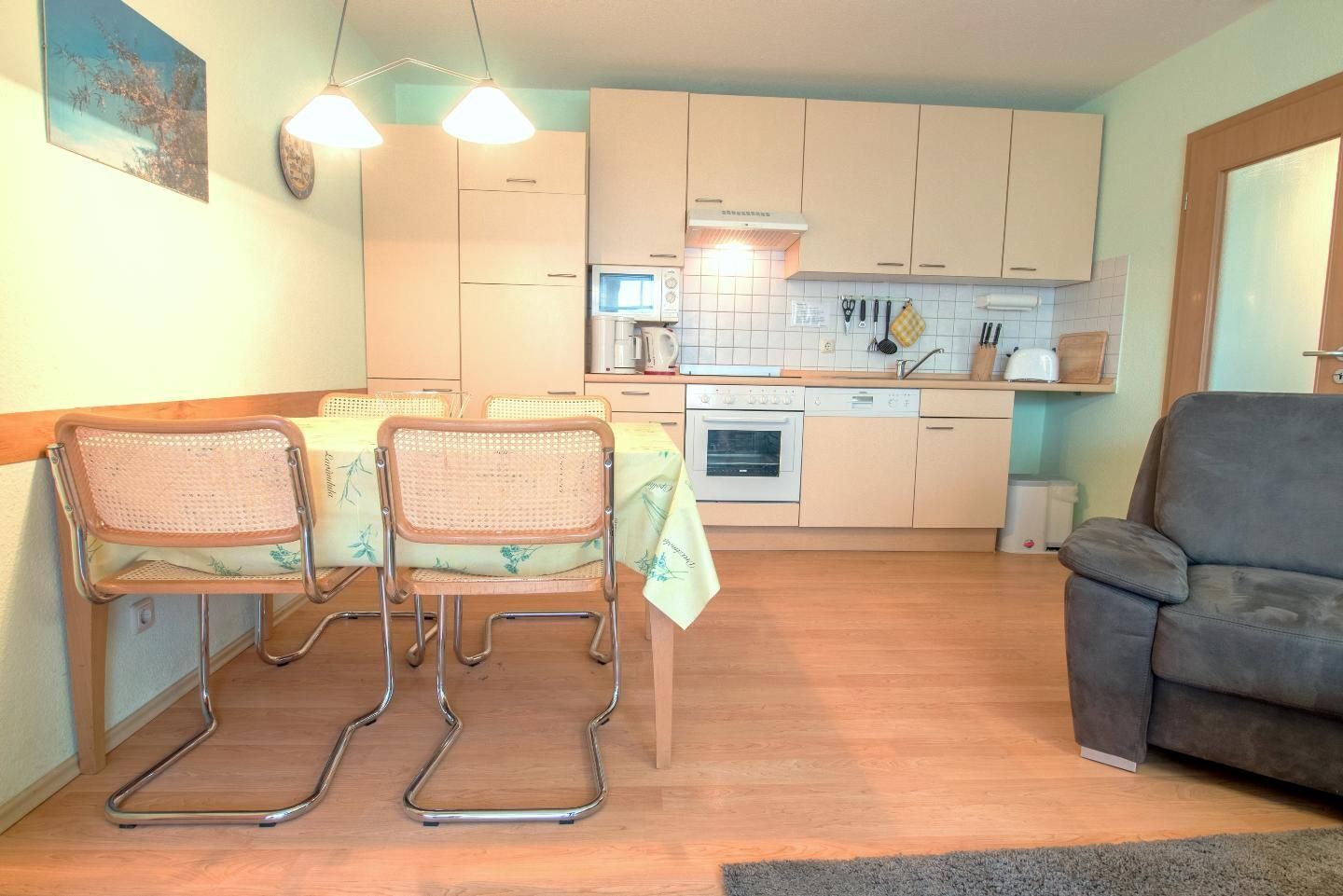 Cocina compacta con zona de comedor, que incluye una mesa con sillas, un sofá y un horno pequeño.