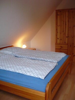 A single bed with a blue mattress and white bedding, a wooden wardrobe, and a nightstand with a lamp. - Comfortable vacation apartment with balcony and parking space near the beach and center - Zur (Zingst)
