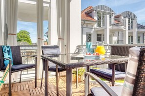A balcony with wicker furniture, a glass table, and a view of a white building with balconies.