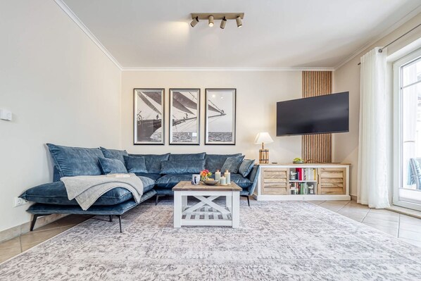 Ein Wohnzimmer mit einem Ecksofa, einem Couchtisch, einem Flachbildfernseher, einem Bücherregal und gerahmten Kunstwerken an der Wand.