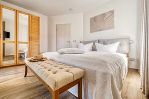 Ein Schlafzimmer mit Bett, Sitzbank, Kleiderschrank und einem an der Wand hängenden Kunstwerk.