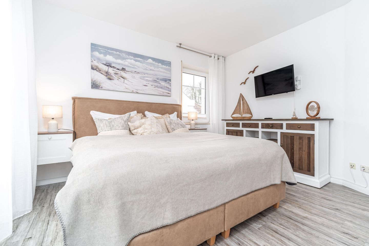 Une chambre à coucher avec un grand lit, un téléviseur fixé au mur, une armoire en bois et une fenêtre avec des rideaux.