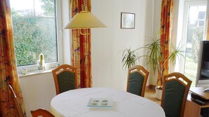 A dining area with a round table, four chairs, a lamp, and a television on a side table.