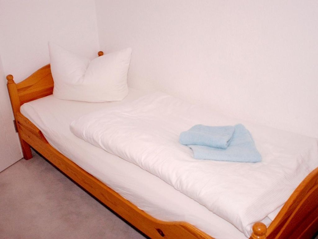 A single bed with a wooden frame, white bedding, and a blue towel.