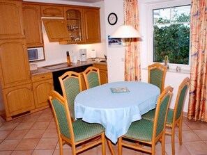 A kitchen with wooden cabinets, a microwave, and a dining table with green chairs.