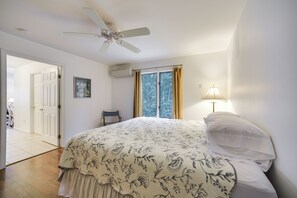 Un dormitorio con cama, ventilador de techo, ventana con cortinas y lámpara de noche.