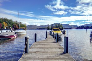 A wooden dock leading to boats on a calm lake with mountains in the background. - Lakefront Adirondacks Home: Fish, Hike, Ski! (Bolton Landing)