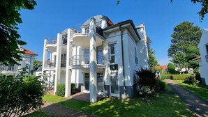 A multi-story residential building with balconies, a brick pathway, and surrounding greenery.